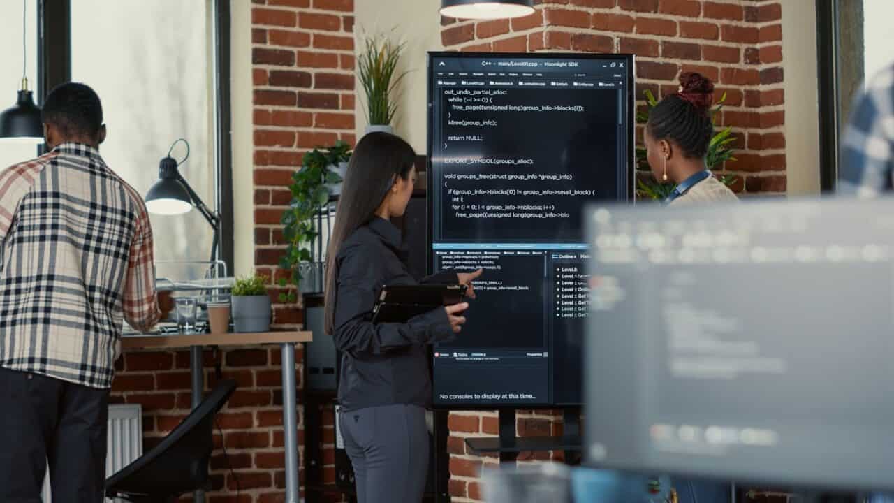 Software engineer holding digital tablet and analyzing code on wall screen